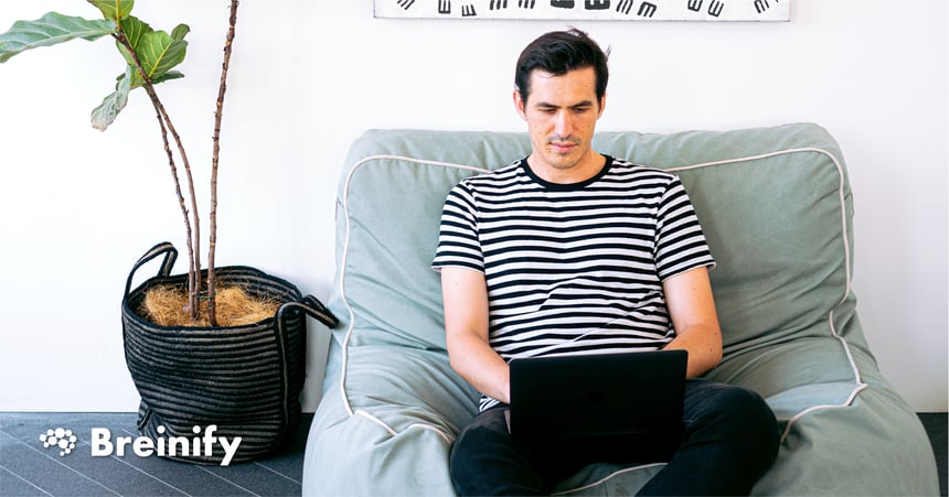 person in striped shirt sitting on a couch with a black laptop