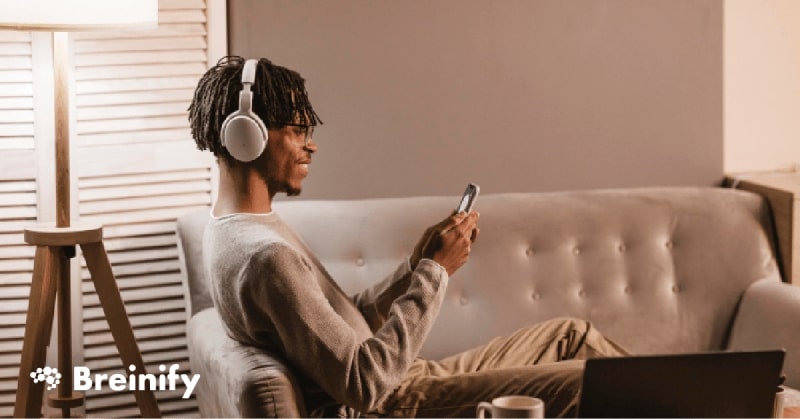 Side view of man with headphones using mobile phone on couch.