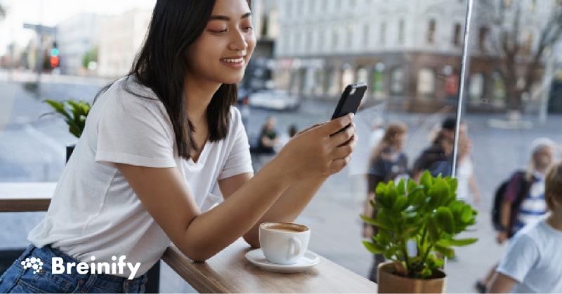 Woman using phone and smiling inside a cafe.