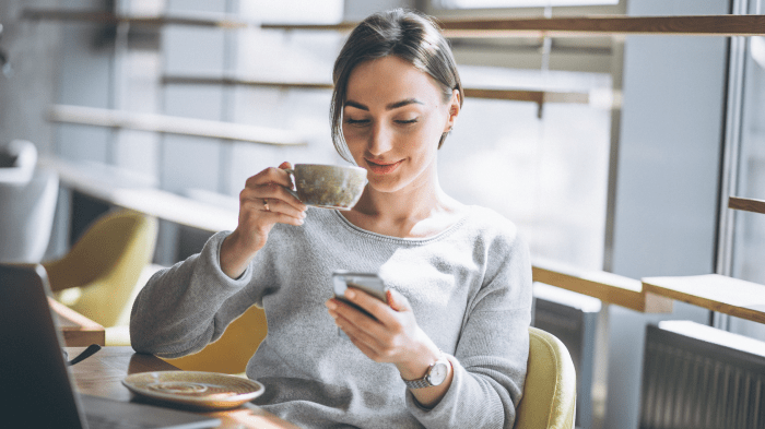 Woman sitting in a chair, shopping online on her phone while drinking tea. 