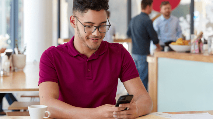 Man wearing red polo shirt sitting in a coffee shop looking on his mobile phone.